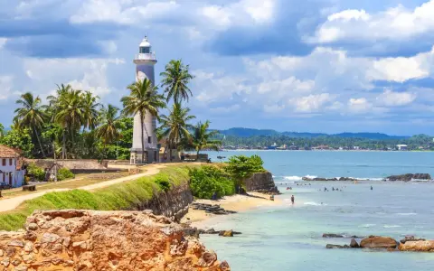 Latarnia morska na Sri Lance, otoczona palmami, z widokiem na ocean i plażę. Idealne miejsce na wakacje, warto sprawdzić wizę Sri Lanka.