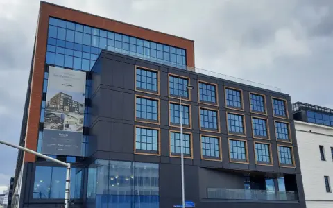 Nowoczesny budynek z cegły i ciemnej fasady, z banerem zapowiadającym otwarcie Occidental Powisle Hotel, części sieci Barceló.
