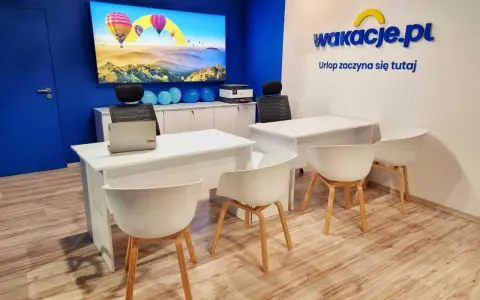 Nowoczesne biuro z logo "wakacje.pl", ekranem z balonami i białymi biurkami.