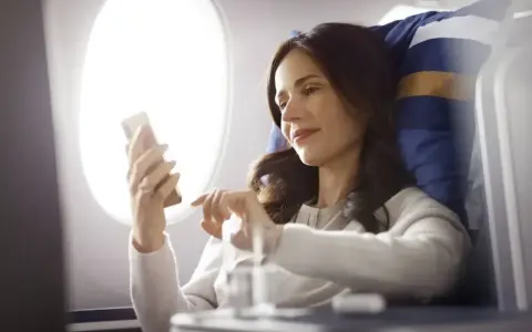 Kobieta korzysta z telefonu, ciesząc się **wifi w samolocie** podczas lotu.