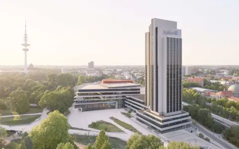 Radisson Blu Hotel w Hamburgu, z wieżą telewizyjną w tle, otoczony zielenią.