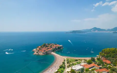 Sveti Stefan, perła Czarnogóry, idealne miejsce na wycieczki. Wyspa z czerwonymi dachami, plaża, turkusowe morze i góry w tle.