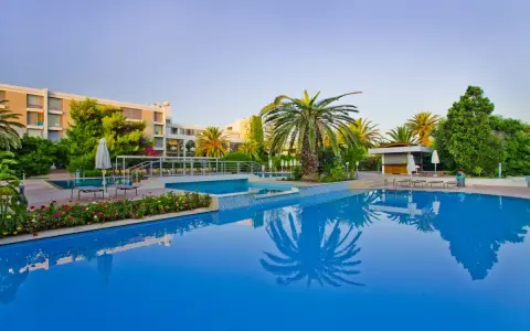 Basen hotelowy z palmami i kwitnącymi kwiatami, idealne miejsce na relaks przy Caravia Beach Kos.