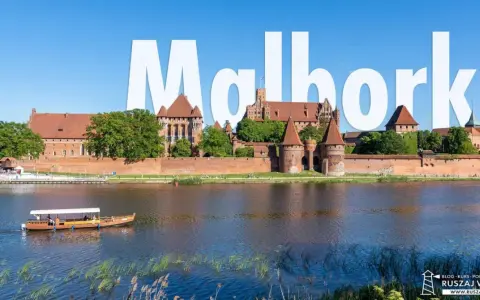 Majestatyczny zamek w Malborku, największy zamek w Polsce, góruje nad rzeką. Stateczek wycieczkowy płynie po wodzie.