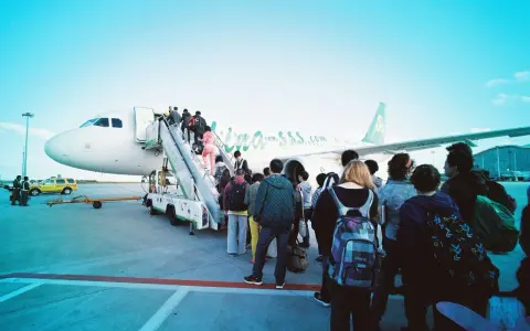Pasażerowie wsiadają do samolotu. W tle widać żółtą taksówkę i personel lotniska. Zapalniczka w samolocie jest zakazana.