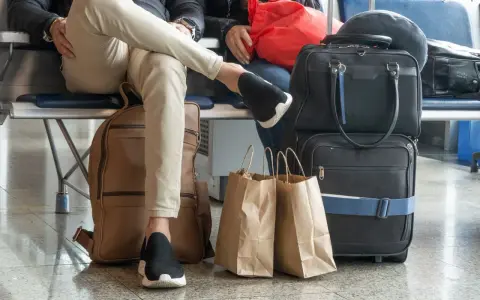 Osoby czekają na lotnisku z bagażem. Widać plecak, torby podróżne i papierowe torby na zakupy. To typowy nouvelair bagaż.
