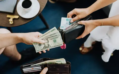 Ręce przekazują sobie pieniądze. Jedna osoba daje dolary, druga wkłada banknoty do portfela. Czy w Turcji można płacić euro?