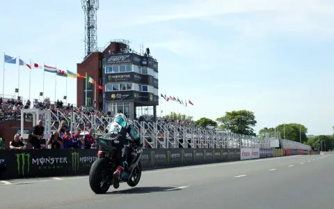 Motocyklista ściga się na wyspie Man, mijając trybuny pełne widzów i wieżę kontrolną.
