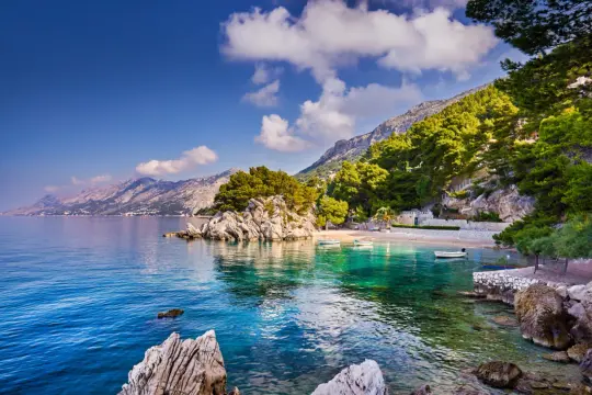 Malownicza zatoczka na riviera Makarska z krystalicznie czystą wodą, skalistymi brzegami i górami w tle.