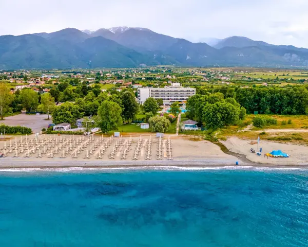 Piękna plaża na Riwierze Olimpijskiej z rzędami leżaków, hotelem i górami w tle.