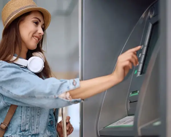 Kobieta w słomkowym kapeluszu i dżinsowej kurtce korzysta z bankomatu.