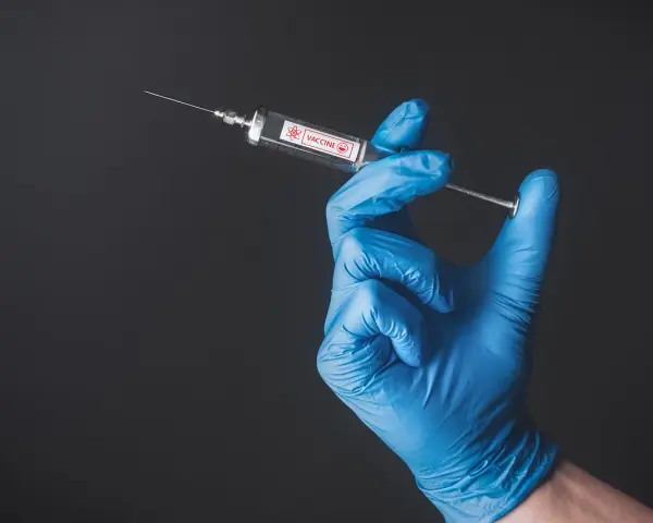 Ręka w niebieskiej rękawiczce trzyma strzykawkę z napisem "VACCINE". To symbol nadziei na bezpieczne podróże, np. do Tunezji, gdzie tunezja szczepienia są kluczowe.