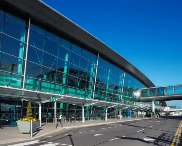 Nowoczesny budynek z przeszkloną fasadą, widoczny jest pas startowy i kładka dla pieszych. To wejście na dublin lotnisko.