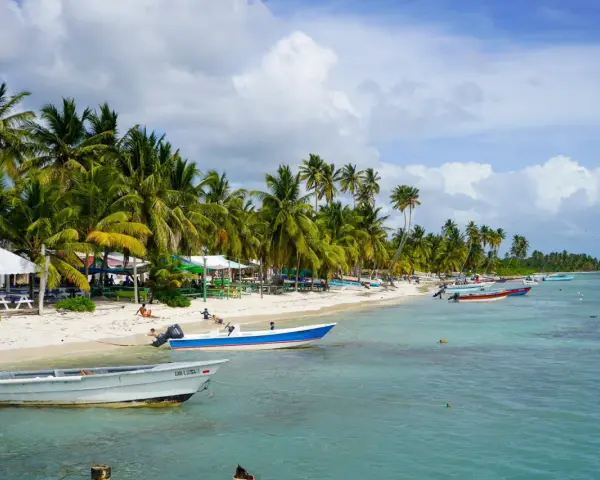 Rajski **Bavaro Beach** z palmami, białym piaskiem, turkusową wodą i łodziami.