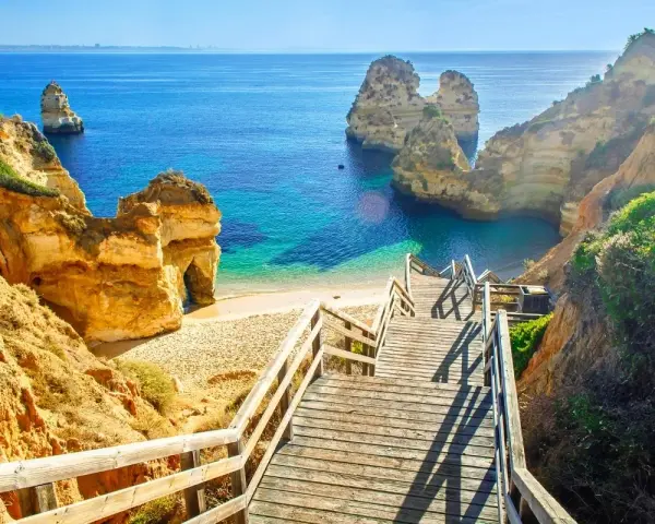 Schody prowadzą na piaszczystą plażę z turkusową wodą i skalnymi formacjami. Idealne miejsce na portugalia wakacje.