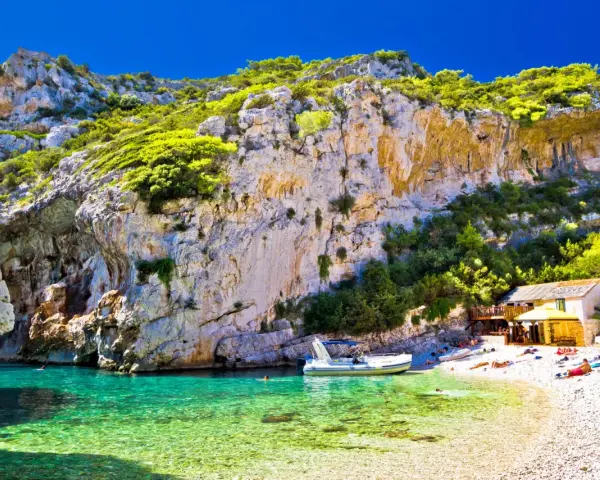 Piękna plaża z krystalicznie czystą wodą i łodzią. Ludzie odpoczywają na kamienistej plaży. Czy Chorwacja jest bezpieczna? Tak, to idealne miejsce na wakacje.