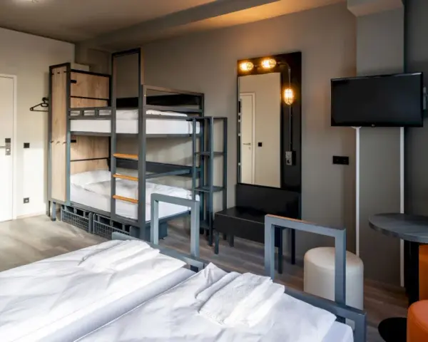 Pokój wieloosobowy w hotelu a&o Warszawa z łóżkami piętrowymi, dwoma łóżkami pojedynczymi i telewizorem.