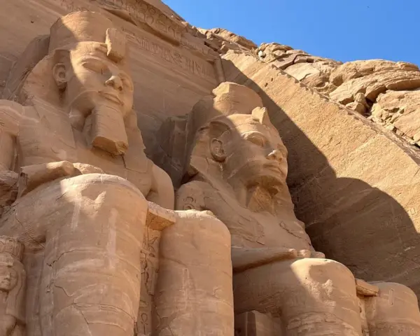 Gigantyczne kamienne posągi faraonów w Abu Simbel, Egipt, na tle skalnej ściany i błękitnego nieba.