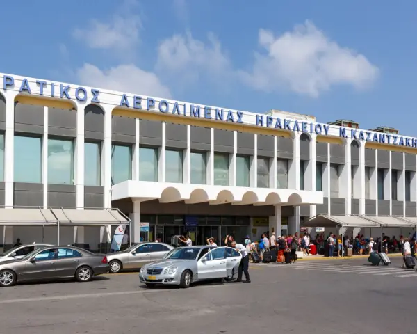 Lotnisko na Krecie, Heraklion N. Kazantzakis. Ludzie z bagażami czekają na transport przed nowoczesnym budynkiem terminalu.
