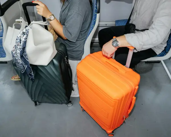 Podróżni z bagażami: zielona walizka, biała torba i pomarańczowa walizka. Jaki bagaż do samolotu?