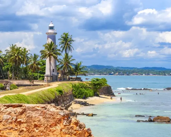 Latarnia morska na Sri Lance, otoczona palmami, z widokiem na ocean i plażę. Idealne miejsce na wakacje, warto sprawdzić wizę Sri Lanka.