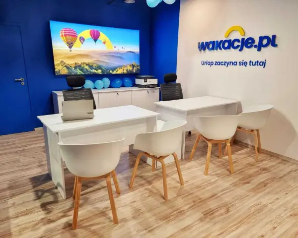 Nowoczesne biuro z logo "wakacje.pl", ekranem z balonami i białymi biurkami.