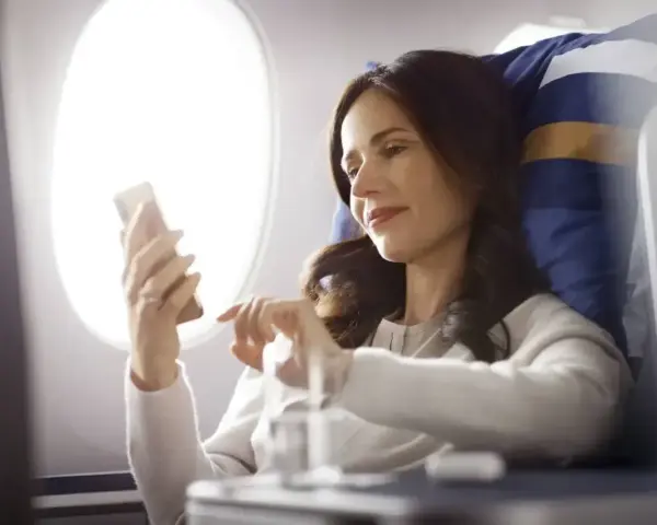 Kobieta korzysta z telefonu, ciesząc się **wifi w samolocie** podczas lotu.