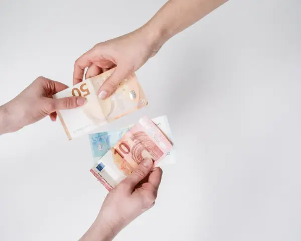 Dwie dłonie przekazują sobie banknoty euro. W Hiszpanii obowiązuje euro, więc to właśnie ta waluta jest tu widoczna.