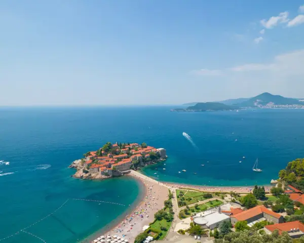 Sveti Stefan, perła Czarnogóry, idealne miejsce na wycieczki. Wyspa z czerwonymi dachami, plaża, turkusowe morze i góry w tle.