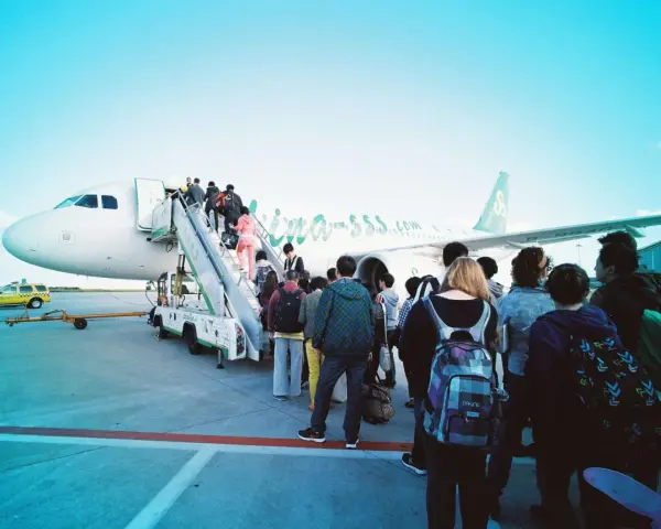 Pasażerowie wsiadają do samolotu. W tle widać żółtą taksówkę i personel lotniska. Zapalniczka w samolocie jest zakazana.