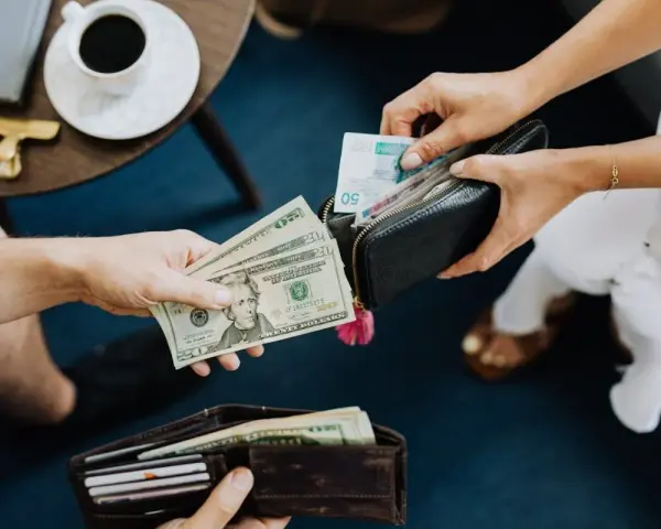 Ręce przekazują sobie pieniądze. Jedna osoba daje dolary, druga wkłada banknoty do portfela. Czy w Turcji można płacić euro?