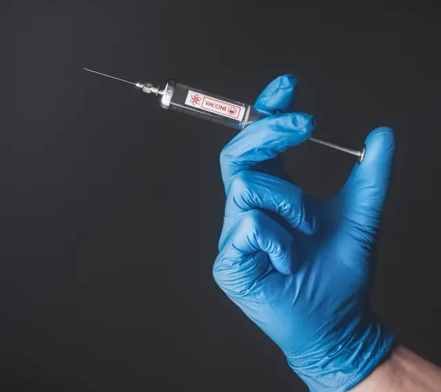Ręka w niebieskiej rękawiczce trzyma strzykawkę z napisem "VACCINE". To symbol nadziei na bezpieczne podróże, np. do Tunezji, gdzie tunezja szczepienia są kluczowe.