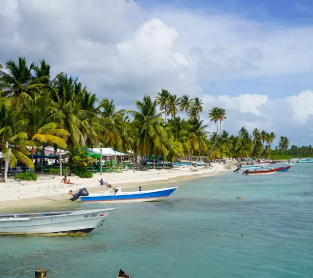 Rajski **Bavaro Beach** z palmami, białym piaskiem, turkusową wodą i łodziami.