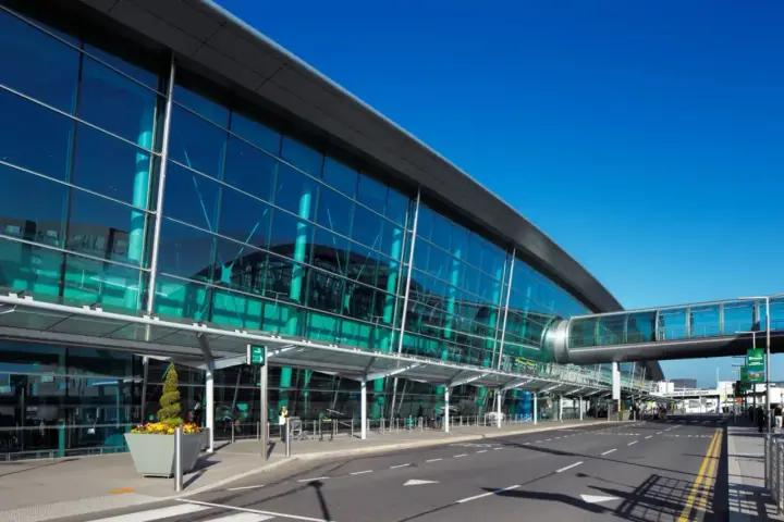 Nowoczesny budynek z przeszkloną fasadą, widoczny jest pas startowy i kładka dla pieszych. To wejście na dublin lotnisko.