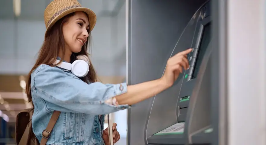 Kobieta w słomkowym kapeluszu i dżinsowej kurtce korzysta z bankomatu.