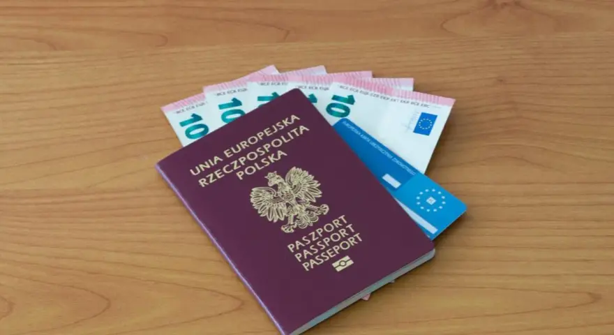 Polski paszport, euro i karta ubezpieczenia zdrowotnego na drewnianym tle.