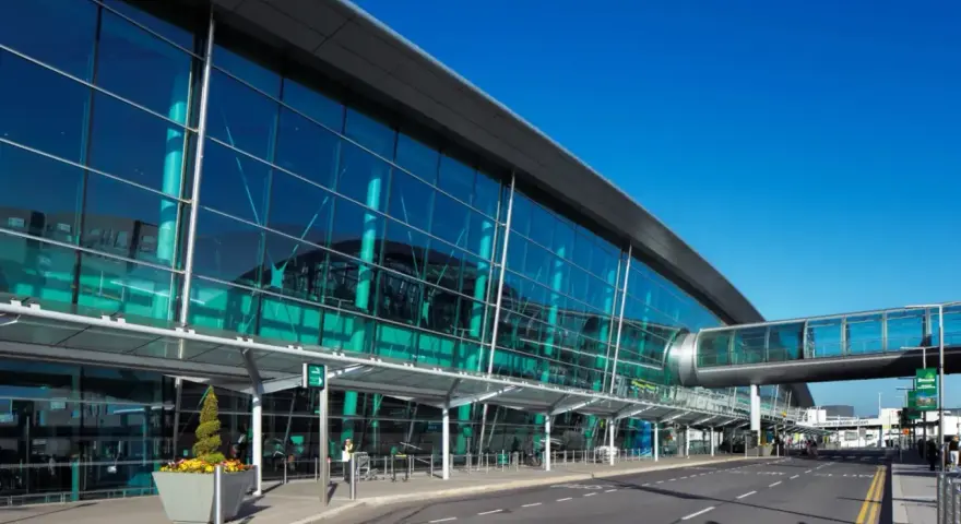 Nowoczesny budynek z przeszkloną fasadą, widoczny jest pas startowy i kładka dla pieszych. To wejście na dublin lotnisko.