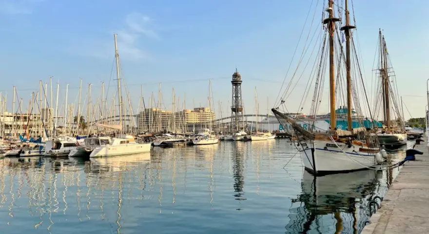 Port w Barcelonie, pełen żaglówek i statków, z wieżą widokową w tle. Czy w Barcelonie jest bezpiecznie? Tak, to spokojne miejsce.
