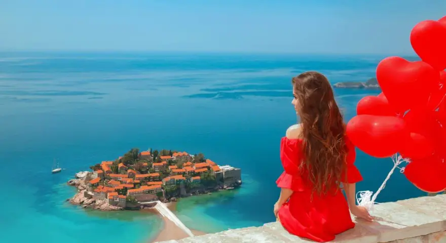 Marzenie o czarnogóra all inclusive samolotem? Kobieta w czerwonej sukni z sercami w ręku podziwia wyspę Sveti Stefan.