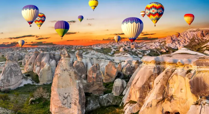 Kolorowe balony unoszą się nad skalistym krajobrazem Kapadocji o wschodzie słońca. Idealne miejsce na wakacje all inclusive!