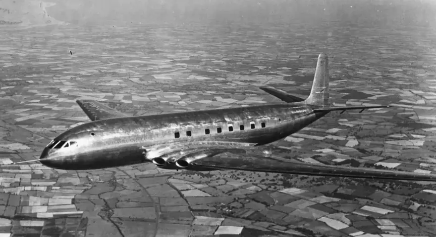 Pierwszy samolot pasażerski, lśniący de Havilland Comet, przelatuje nad patchworkiem pól.