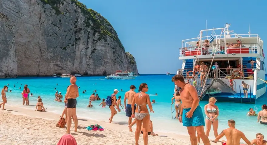 Tui promocje na wakacje: ludzie na plaży Navagio, Zakynthos, Grecja. Turkusowa woda, biały piasek i klify.