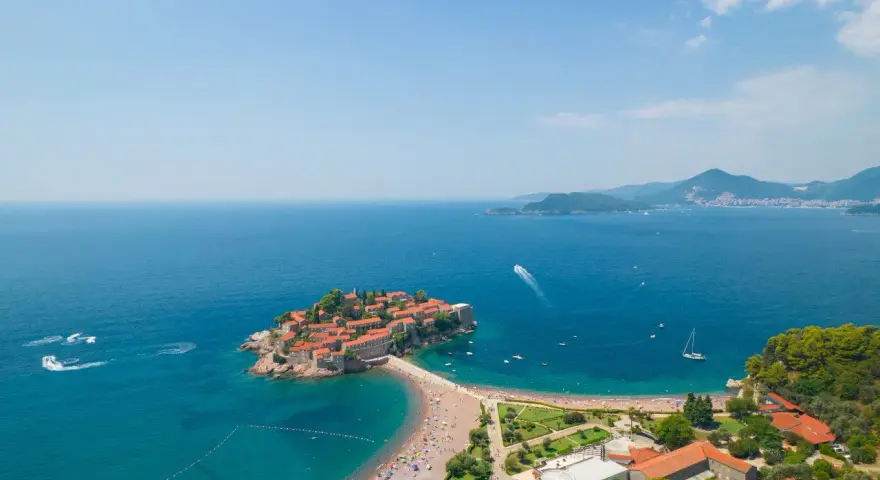 Sveti Stefan, perła Czarnogóry, idealne miejsce na wycieczki. Wyspa z czerwonymi dachami, plaża, turkusowe morze i góry w tle.