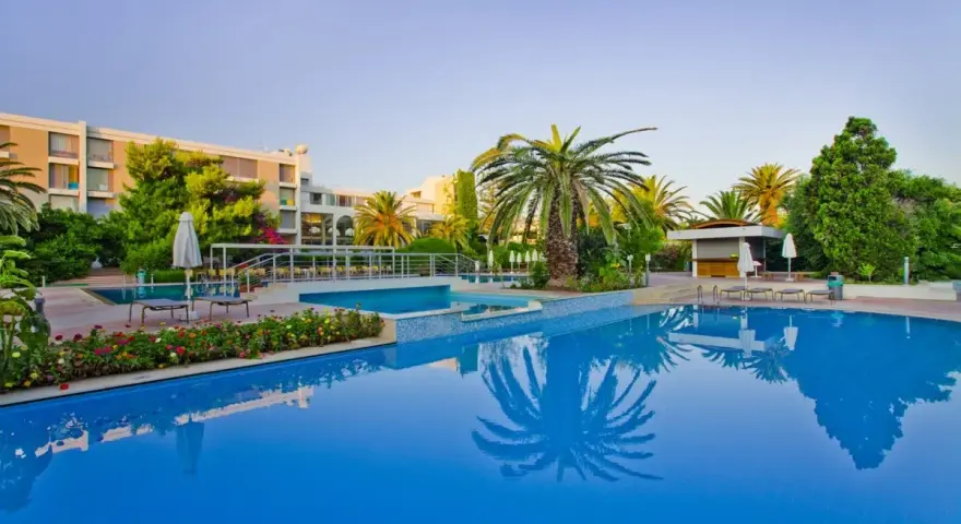 Basen hotelowy z palmami i kwitnącymi kwiatami, idealne miejsce na relaks przy Caravia Beach Kos.