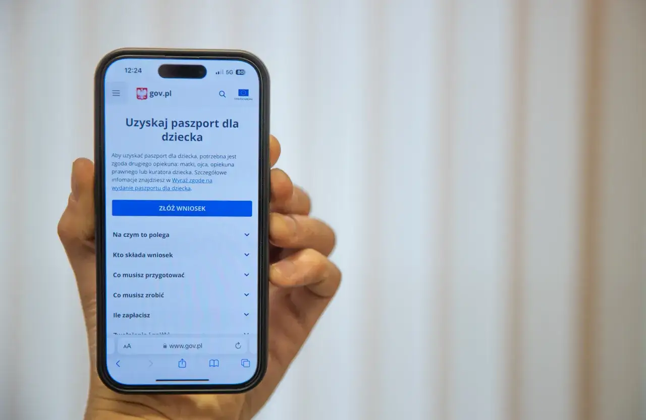 Dłoń trzyma smartfon z otwartą stroną gov.pl, gdzie można złożyć wniosek o paszport dla dziecka online.