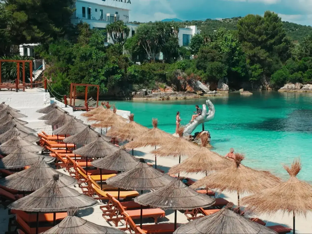 Idealne miejsce na spontaniczny wyjazd last minute do Albanii. Słoneczna plaża z leżakami i parasolami, turkusowa woda i unikalna rzeźba dłoni.