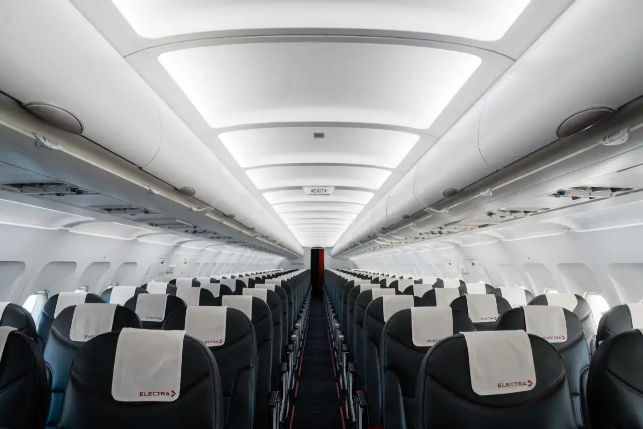 Puste wnętrze samolotu linii lotniczych Electra Airways z rzędami czarnych foteli i białymi zagłówkami z logo.
