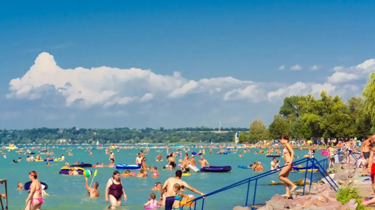 Tłum ludzi cieszy się latem na plaży nad jeziorem Balaton. Woda jest pełna kąpiących się, pływających na materacach i bawiących się.