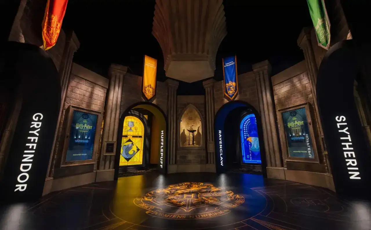 Witaj w muzeum Harry'ego Pottera! Wielkie herby domów Hogwartu na podłodze i banery zapraszają do wejścia.