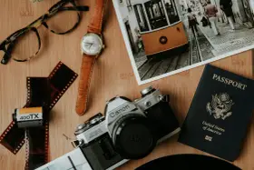 Paszport USA, aparat Canon, klisza, zegarek i okulary na drewnianym tle. Kto wydaje paszport? Rząd USA.